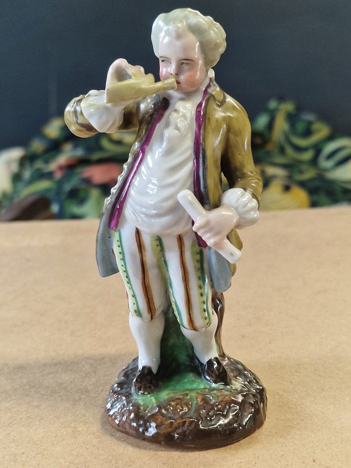 The porcelain gentleman uncensored: playing a little horn, with his flute tucked under his arm.
